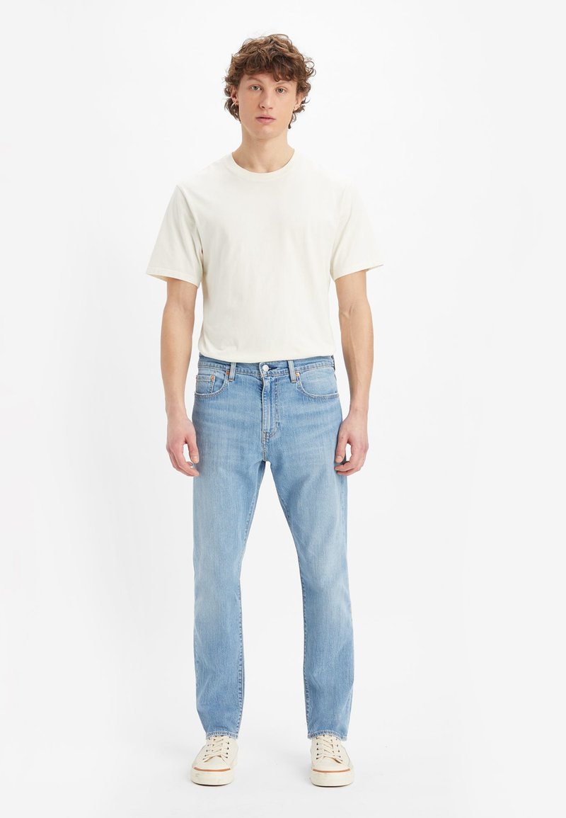 Lightweight beige t-shirt and light blue straight-leg jeans. Features a classic design with subtle stitching and standard hardware accents.