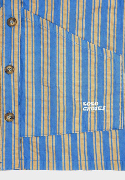 Poche de chemise à rayures verticales bleues et jaunes avec des boutons marron et le texte brodé en blanc "POLO CHOICES" sur le tissu.