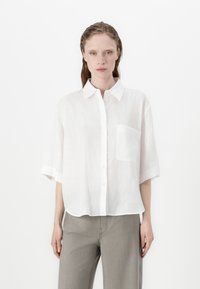 White short-sleeve shirt made of lightweight fabric. Features a button front, collar, and single chest pocket. Clean, minimal design.