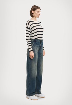 Striped black and white sweater paired with loose-fitting, faded blue jeans and white sneakers. Texture is soft and denim is slightly worn.