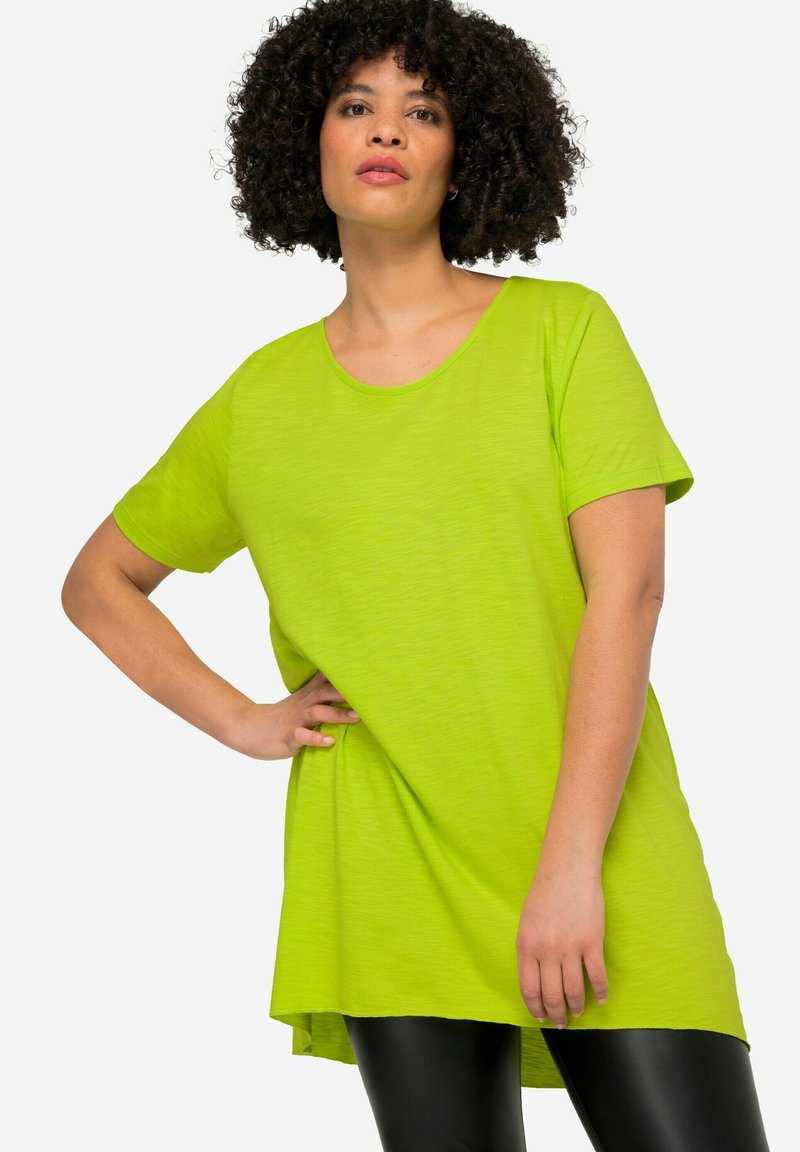 Limetkově zelené oversized tričko z lehké texturované tkaniny s kulatým výstřihem a krátkými rukávy, doplněné černými legínami.