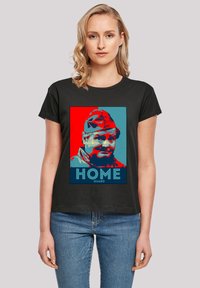 Schwarzes T-Shirt mit kurzen  Ärmeln, das einen grafischen Druck eines Männerporträts in Rot und Blau zeigt, mit dem Text "HOME GUARD" am unteren Ende.