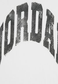 T-shirt bianca con grande testo nero "JORDAN" in un font grassetto e leggermente usurato, con un motivo a punti per la texture.