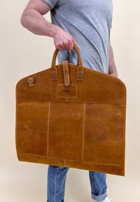 Braune Ledertasche mit zwei oberen Griffen, die eine große rechteckige Form aufweist, sichtbare Nähte und eine markante glatte Textur hat.