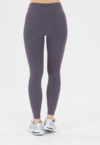 Lila högmidjade leggings tillverkade av elastiskt tyg, med en jämn yta. Bärs tillsammans med silverfärgade träningsskor.