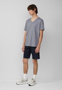 T-shirt gris mélangé à manches courtes et col en V associé à un short en denim foncé et des chaussures de course claires, affichant une tenue sporty et décontractée.