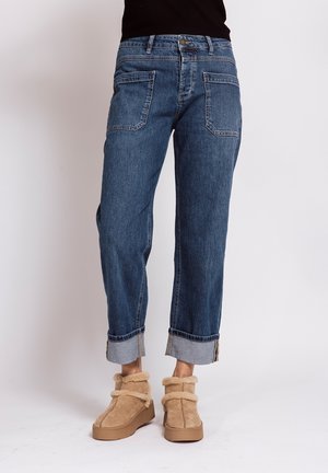Woman wearing rolled-up blue jeans and beige fur-lined ankle boots against a plain background.