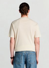 Cremefarbenes, geripptes Kurzarmshirt mit rundem Ausschnitt, kombiniert mit hellblauen Jeans. Minimalistisches Design mit dezenter Textur.