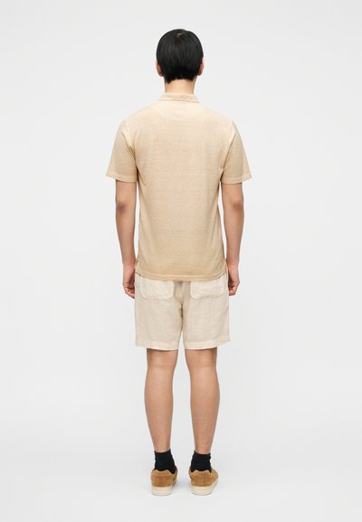 Μπεζ κοντομάνικο πόλο από μαλακό ύφασμα, συνδυασμένο με ανοιχτό μπεζ λινό σορτς, με δύο πίσω τσέπες. Casual εμφάνιση με σκουρόχρωμες κάλτσες.