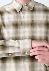 Camicia a quadri in tonalità beige e crema, con colletto button-down e bottoni ai polsini, caratterizzata da una texture liscia e tessuta.
