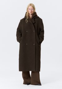 Brown wool double-breasted coat with a large collar, side pockets, and a relaxed fit, worn over a matching brown outfit.