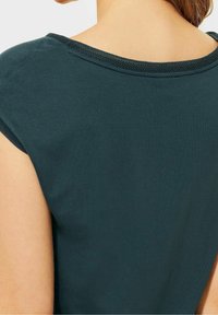 Dark teal cotton shirt with a rounded neckline, short sleeves, and subtle texture in the fabric. Minimalist design with clean lines.