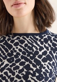 Marineblauwe blouse met een witte luipaardprint, voorzien van een ronde halslijn en een gladde textuur, gepositioneerd boven de sleutelbeen.