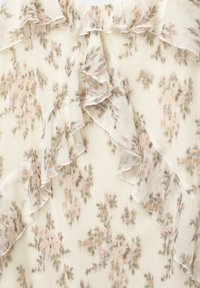 Tejido de gasa floral con suaves tonos rosas y verdes. El diseño incluye delicados volantes a lo largo de los bordes y una textura ligera y translúcida.