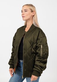 Giacca bomber trapuntata verde oliva realizzata in tessuto morbido. Caratterizzata da polsini a coste, zip frontale e una tasca sulla manica sinistra.