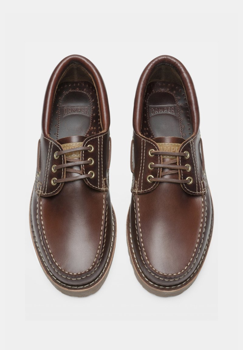 Une paire de chaussures décontractées en cuir marron à lacets avec des coutures visibles et des semelles intérieures marquées sur un fond blanc.