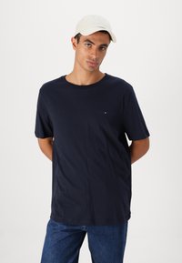 Marineblå bomulls t-skjorte med rund hals og korte ermer, med en liten logo på brystet, kombinert med blå denimjeans.