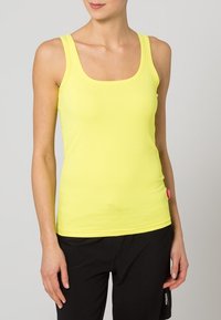 Gul ribbad tanktopp med fyrkantig halsringning, smala axelband och en figurnära design. En liten rosa etikett är synlig vid fållen.