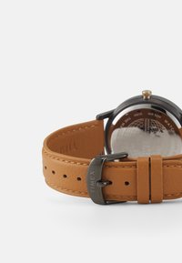 Nahatava nahkrihmaga käekell pruuni rihmaga, hõbedase korpusega ja selge tagaküljega, mille kaudu on näha mehhaanilisi detaile. Sanga peal on graveeritud "TIMEX".