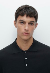 Polo noir avec un col classique et une patte de boutonnage à trois boutons. Texture de tissu lisse, design ajusté et fond uni.