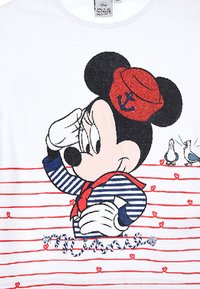 Camiseta blanca de manga corta que presenta un personaje de dibujos animados con un sombrero de marinero rojo con un ancla, una camiseta de rayas azul y blanca, y acentos rojos en forma de corazón.