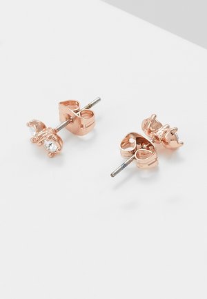 Boucles d'oreilles clous en or rose avec petites pierres claires et tiges métalliques reposant sur une surface blanche.