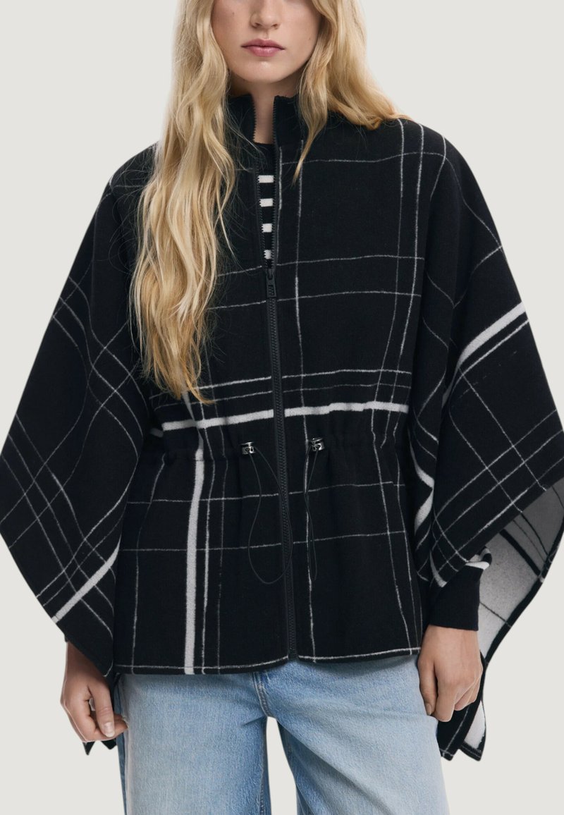 Cappotto a scacchi bianco e nero con zip frontale, vita con cordino e maniche ampie. Tessuto morbido con una consistenza accogliente.