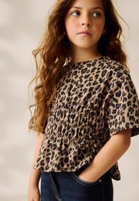 Leopardprint kortærmet top med samlede detaljer i beige og sort, parret med mørkeblå denim jeans. Blød stofstruktur.