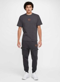 Mörkgrå kortärmad t-shirt med orange Nike-logotyp, i kombination med matchande cargobyxor som har flera fickor och elastiska muddar, bärs med vita sneakers.