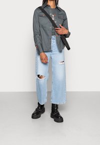 Gray button-up jacket, distressed light blue wide-leg jeans, black chunky boots, and a crossbody bag with a smooth texture.