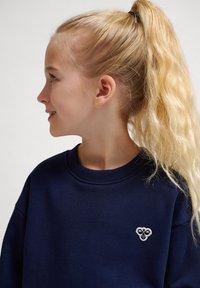 Mörkblå sweatshirt med rund hals, som har en liten broderad logotyp på bröstet. Materialet verkar mjukt med en strukturerad yta.