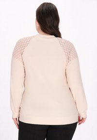 Helles rosa Sweatshirt mit strukturiertem Oberteil und Spitzenakzenten an den Schultern. Lange Ärmel und gerippte Bündchen sowie Saum. Glattes, weiches Material.