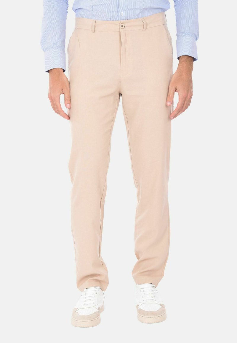 Pantaloni beige realizzati in tessuto leggero con vestibilità dritta, dotati di due tasche laterali e chiusura con bottone. Indossati con sneakers bianche.