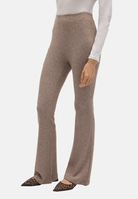 Pantalones acampanados de canalé marrón, confeccionados en un material suave, con una cintura alta y una textura lisa. Combinados con planos de leopardo negro de punta.