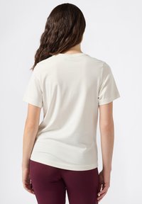 Hellbeige T-Shirt mit kurzen Ärmeln aus glattem Stoff, mit Rundhalsausschnitt und weiter Passform, kombiniert mit bordeauxfarbenen Leggings.