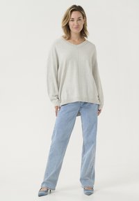 Jasnoszary, oversize sweter z dekoltem w szpic, długimi rękawami i bocznymi rozcięciami, zestawiony z jasnoniebieskimi dżinsami prostymi oraz niebieskimi szpilkami.