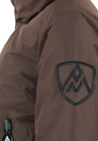 Manche de veste marron avec patch de logo de montagne brodé noir et petite tirette zippée noire avec détail de logo assorti.