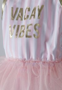 Ružovo-biele pruhované tkanivo so zlatým textom "VACAY VIBES". Obsahuje vrstvenú sukňu z ružového tylu s volánovým lemom v páse.