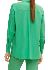Camicia verde a maniche lunghe realizzata in tessuto morbido, con colletto, polsini con bottone e spacchi laterali, caratterizzata da una vestibilità rilassata e dettaglio della yoke posteriore.