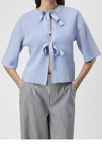 Jasnoniebieski sweter z dzianiny z okrągłym dekoltem, wiązaniem z przodu i krótkimi rękawami, zestawiony z szerokimi spodniami w paski.