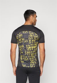 Camiseta atlética negra con un patrón gráfico amarillo, mangas cortas, cuello redondo y una silueta ajustada, fabricada con un material suave y elástico.