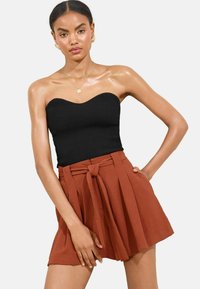 Zwarte geribbelde strapless top gecombineerd met een roestkleurige geplooide rok met een gestrikte tailleband. Gladde textuur met duidelijke lijnen.