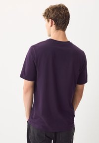 Kortærmet lilla bomuldst-shirt med rund hals, med en glat tekstur og en klassisk pasform, vist bagfra.