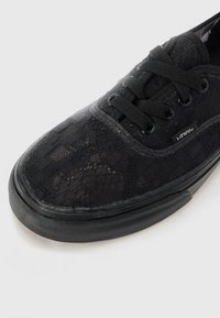Black lace sneaker with a textured pattern, round toe, black laces, and rubber sole. Features a small logo on the side.