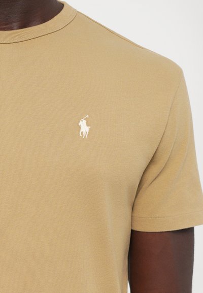 Μπεζ βαμβακερό T-shirt με κοντά μανίκια, ριμπ λαιμόκοψη και μικρό λευκό κεντητό λογότυπο στο αριστερό στήθος. Μαλακή υφή και εφαρμοστή σχεδίαση.