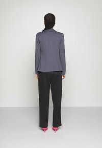 Dopasowana szara marynarka o eleganckiej sylwetce, zestawiona z luźnymi czarnymi spodniami i różowymi szpilkami, widziana od tyłu.