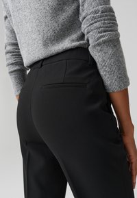 Pantaloni neri su misura con una texture liscia, dotati di una tasca posteriore, abbinati a un maglione grigio con texture e maniche a costine.
