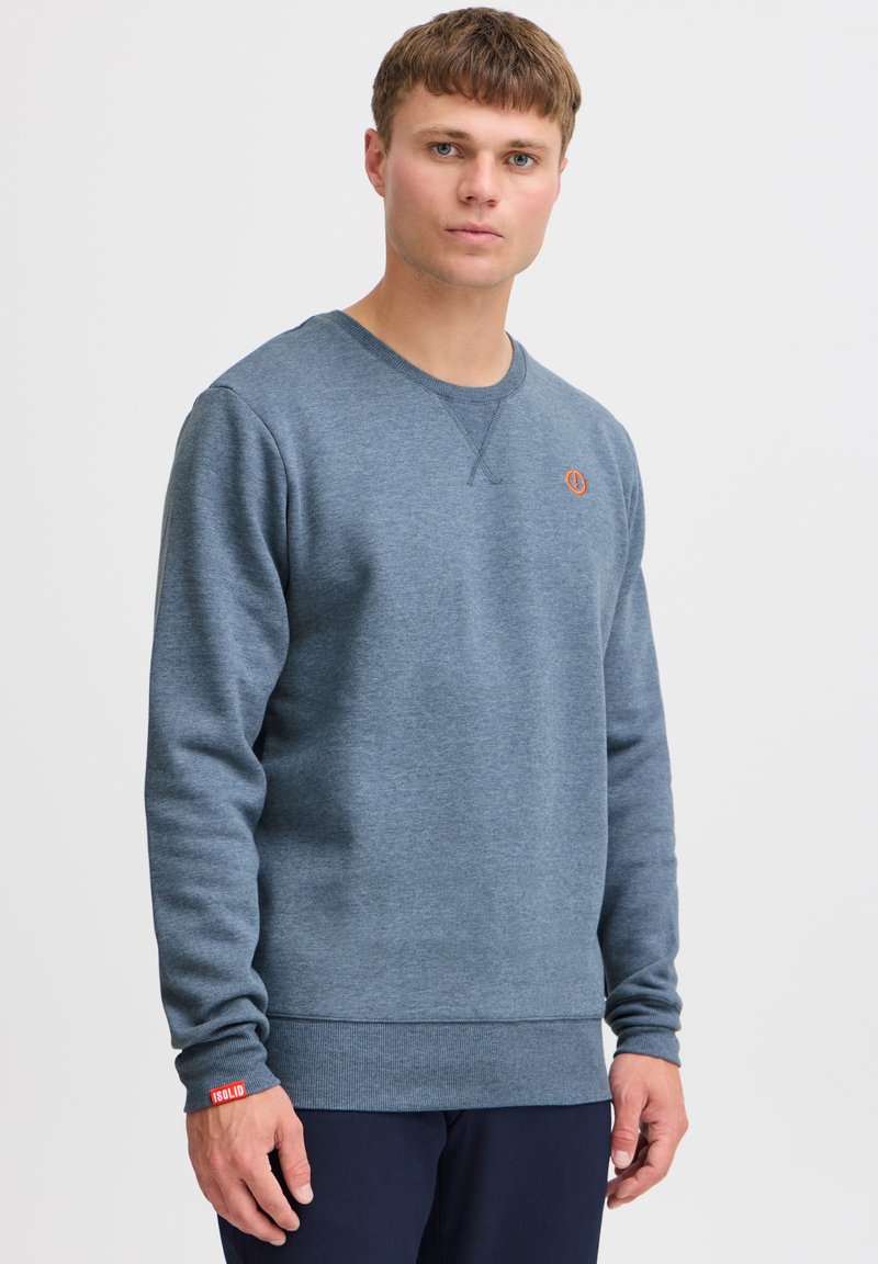 Blå sweatshirt lavet af blødt stof, med rund halsudskæring, ribbede ærmer og kant, samt et iøjnefaldende orange logo på brystet.