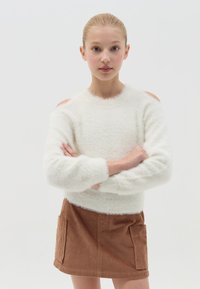 Weißer, flauschiger Pullover mit gerippten Bündchen, kombiniert mit einem braunen Cordrock mit zwei Seitentaschen und geradem Saum.