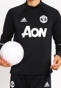 Musta pitkähiha joukkuepaita, jossa on valkoinen "Aon" -logo ja Manchester Unitedin embleemi. Hihassa on Adidas-raidat. Pitää valkoista jalkapalloa.